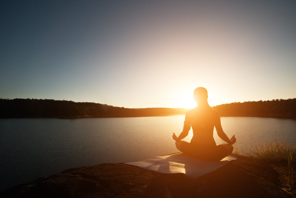 Healthy woman practicing yoga at mountain lake during sunset.