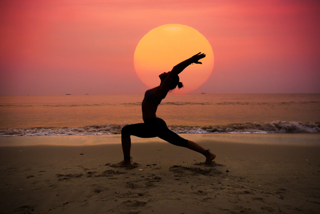 Young woman practicing yoga on beach at sunrise.